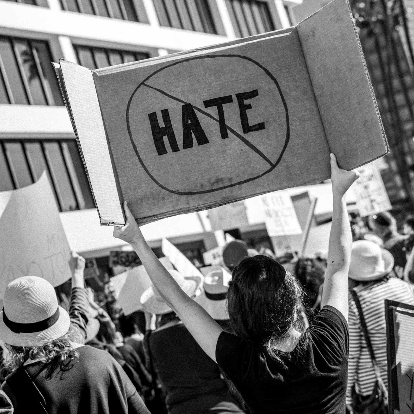 A person holding a cardboard sign with the word HATE crossed out, in a crowd