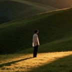 A lone figure standing on a sunlit slope among rolling green hills